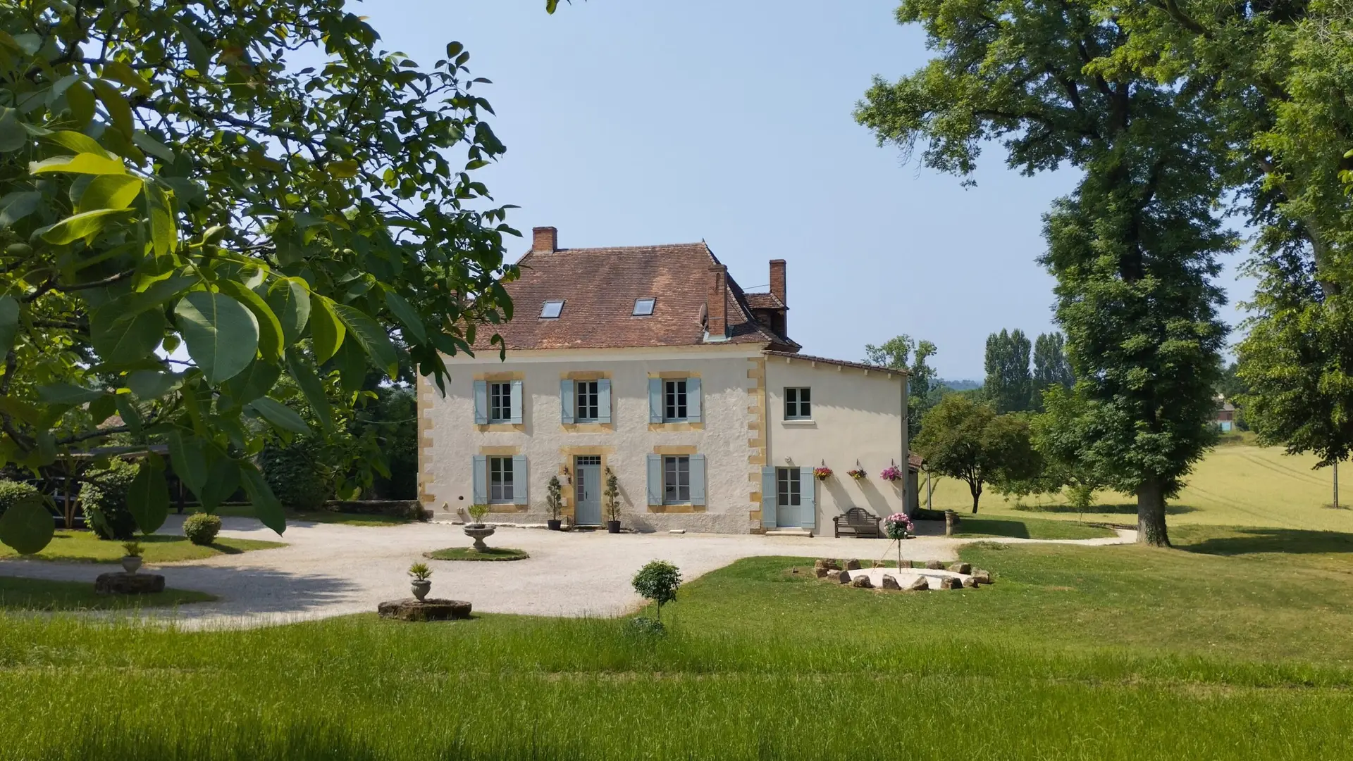 Landscape image of front of Manoir showing drive, tall trees either side edging onto the walnut trees to the side